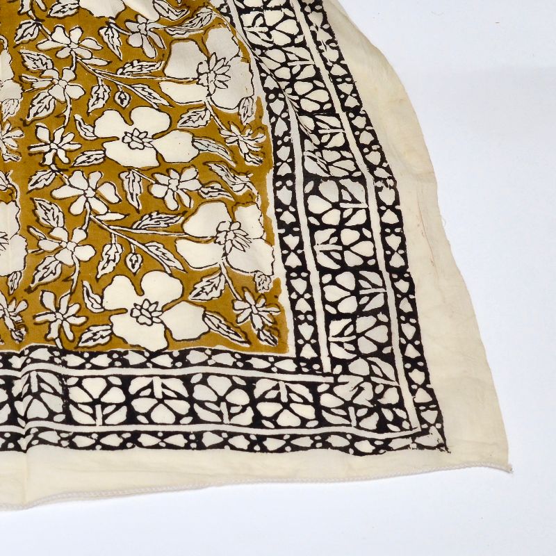 Hand block printed on organic cotton Pareo Beach Sarong with a mustard yellow base, intricate white floral patterns, leafy motifs, and a bold black and white geometric border, showcasing traditional craftsmanship for a stylish, eco-friendly beach accessory.