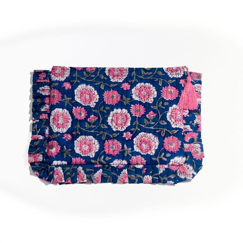 A handcrafted makeup bag with a deep blue fabric cover, featuring an intricate pattern of pink floral embroidery with green vines and leaves, accented by a ruffled edge and a pink tassel, set against a plain white background.