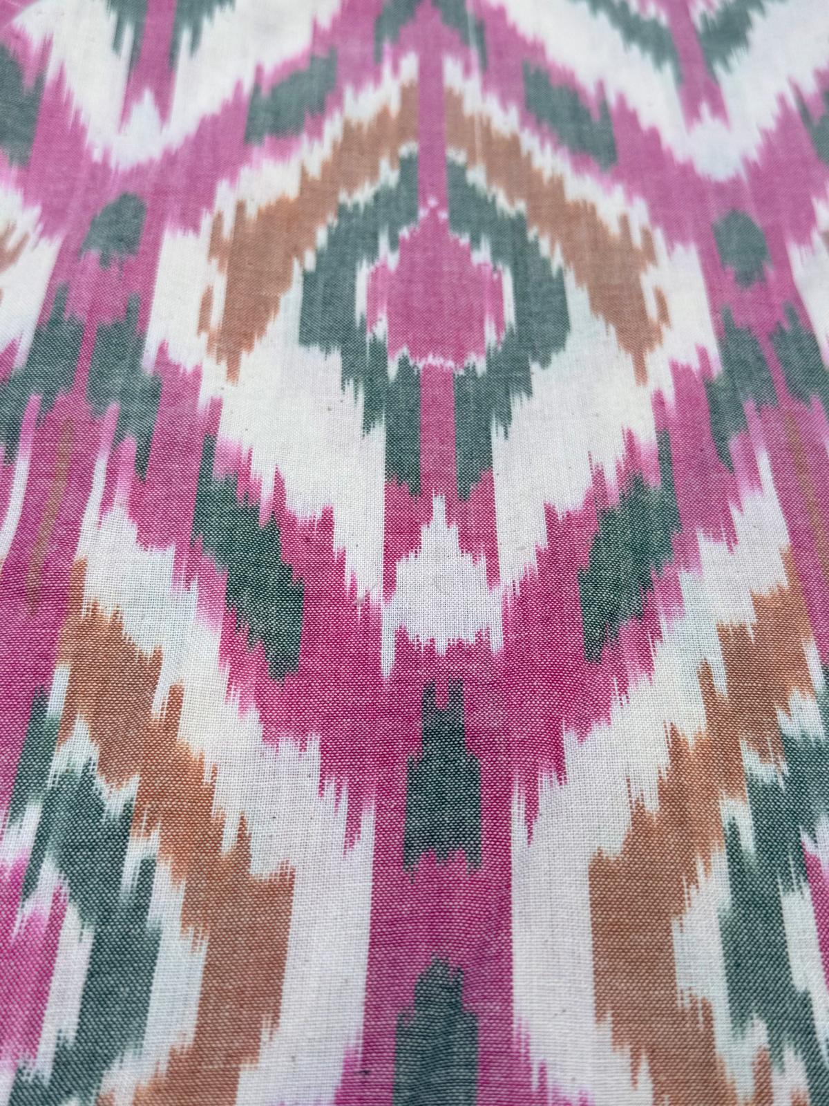 A detailed macro view of hand-loomed ikat textile showcasing woven geometric patterns in vibrant magenta, sage green, tan, and soft cream threads.