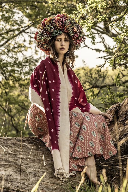 model sits barefoot on a log wearing a pink wrap skirt and shawl.